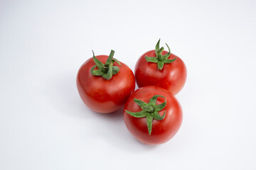 Three fresh red tomatoes with green leaves on white background.