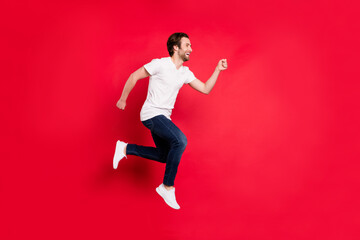 Fototapeta na wymiar Full size profile photo of young brown hairdo man run wear white t-shirt jeans isolated on red color background