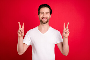 Photo of funny young brown hairdo man show v-sign wear white t-shirt isolated on vivid red color background