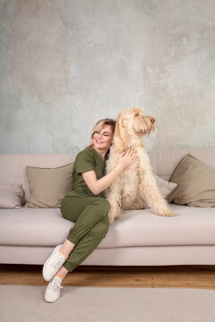 young beautiful woman with cute spinosa dog in the room. She wears vet uniform