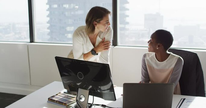 Two diverse female colleagues looking at laptop and discussing in office