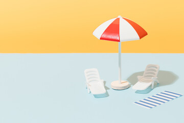 White and red beach umbrella, sun chairs and blue and white striped towel on blue and yellow...