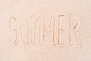 the word summer written with the finger on a sandy beach background. concept of summer and holidays. copy space.