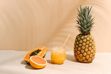 a refreshing glass of fruit juice with a straw next to a pineapple, half a papaya and half an...