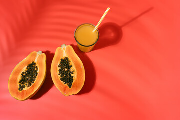fresh papaya with black seeds and a glass of fruit juice with straw on a red background with...