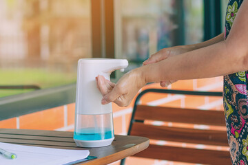 Obraz premium Automatic alcohol dispenser for cleaning hand to prevent the spreading of Coronavirus (Covid-19) on table before entrance to cafeteria. Healthcare concept. New normal lifestyle. Selective focus