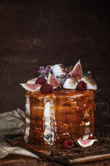 Caramel cake with wild berries, cream and figs on brown background