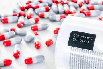 Expired date and lot number label print on medicine bottle with blurred background of pile of old red-grey painkiller pills on table, awareness expiration information from pharmaceutical manufacturing - obrazy, fototapety, plakaty