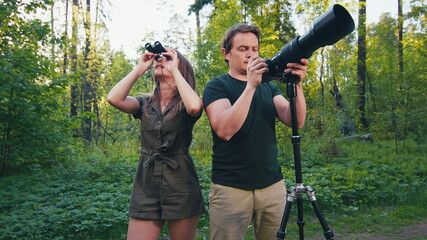 Birdwatching in park. Couple watch birds with binoculars and camera with telephoto lens. Amateur...