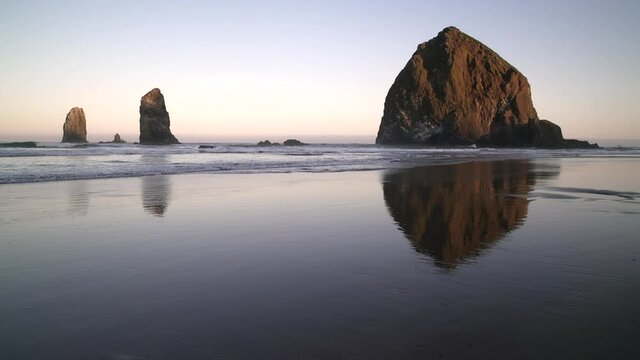 Beach Dawn Haystack Rock Cannon Beach 4K UHD. Sunrise at Haystack Rock in Cannon Beach, Oregon as the surf washes up onto the beach. United States.
