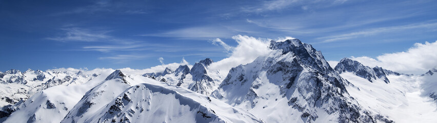 Panorama of high snow-capped mountain peaks and beautiful blue sky with clouds - 435877282