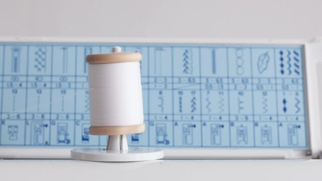 Close up of a spool with white thin thread on working a new sewing machine. Spool with thin white thread on working a sewing machine.