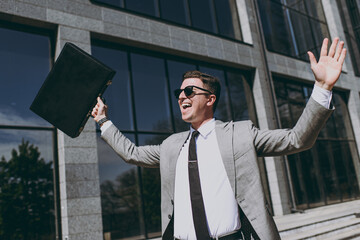 Young overjoyed winner successful happy employee business man 20s in grey suit walking go near...