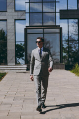 Full length young confident serious employee business man 20s wearing grey suit walking go near...