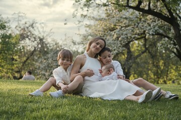 Fototapeta premium Mother and three children hugging. Happy family sitting outdoor: woman and two brother kids boys and cute little toddler boy