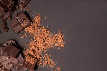 Composition of bars and pieces of different milk and dark chocolate, grated cocoa on a black background top view close up