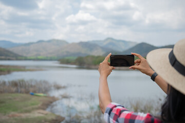woman stand on the banks of the lake using her cell phone send message sms e-mail, taking pictures, Video call, Asian woman hiker in front smiling happy, Woman hiking in woods, warm summer day.