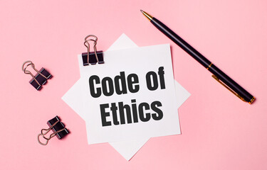 On a light pink background, black paper clips, black pen and white note paper with the words CODE OF ETHICS. Flat lay