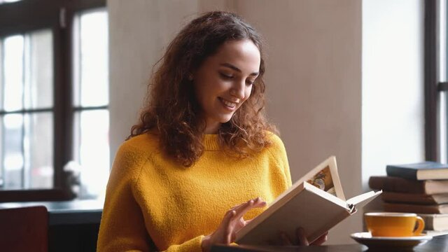 A beautiful woman is reading a book sitting in the cafe inside