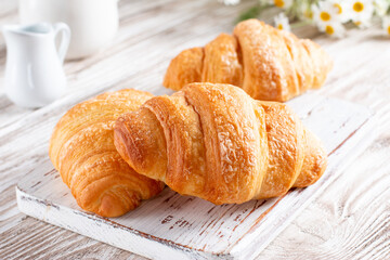 Freshly baked croissants on light wooden board. French pastry.