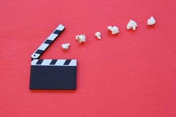 Film clapperboard and popcorn isolated on red background. Entertainment industry. Movie time....