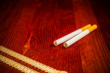 Cigarettes and a gold chain on a table in mahogany