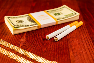 Cigarettes and a gold chain with money on a table in mahogany