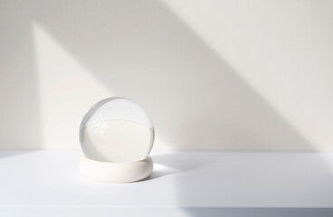 Minimal composition with glass ball on white desk, glass globe ball as decoration of interior. Abstract shadow lines on the wall, space for text, mockup