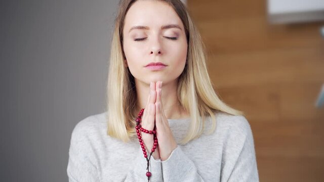 portrait young girl or woman sincerely praying on rosary at home. Prayer of repentance. Female believer with closed eyes and a beads in his hands. Christian or Orthodox Catholic in daily prayers