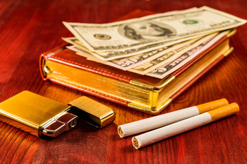 Leather diary and cigarettes with golden lighter and money on a mahogany table. Focus on the cigarettes