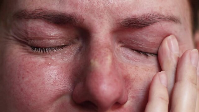 Woman is crying. Upset depressed girl with colorful eyes and tears on cheeks alone at home. Tears are flowing.