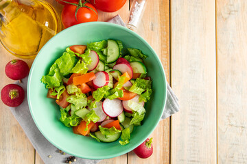 Fresh vegetable salad with olive oil in ceramic bowl on wooden background. Seasonal summer dish of tomatoes, cucumbers and radishes.