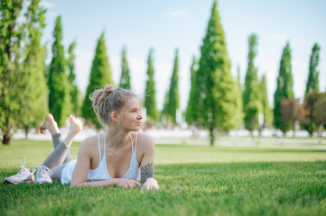 Attractive sportive girl lies on the grass and relaxes in park