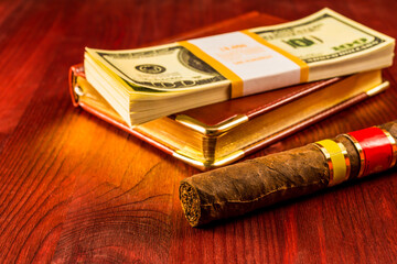 Pack of dollars with a leather diary and cuban cigar on a mahogany table