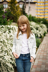 Obraz premium smiling girl in a white denim jacket near a flowering white bush