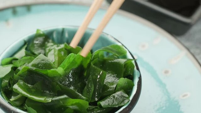 Eating algae with chopsticks. Soaked wakame seaweed in a bowl. Japanese food. Healthy seafood.