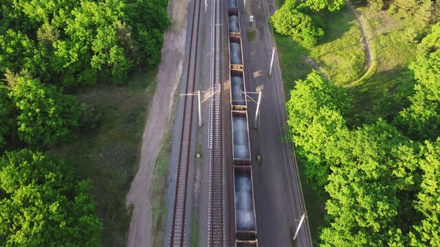 Aerial view of railroad with train in sunny summer day in forest. Top view of cargo with industrial products. Logistics, trade, shipping concept