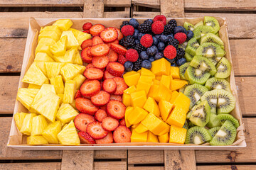 large tray of chopped assorted fruits with pineapple, mango, kiwi, strawberries and red berries in...
