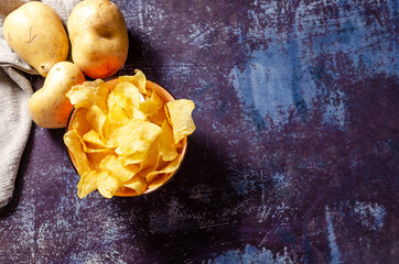 Still life of a bowl of potato chips with raw potatoes and a linen cloth.