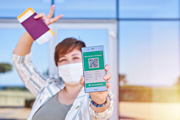 Happy woman holding smartphone displaying on app mobile valid digital vaccination certificate for...