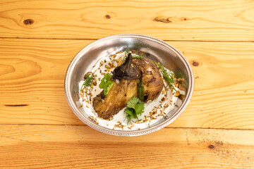 Photo of a beautiful metal bowl with roasted aubergines and yogurt cream with coriander, seeds