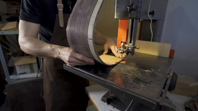Anonymous luthier cutting guitar body on bandsaw in workroom