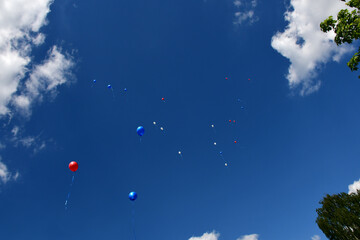 White, blue and red balloons fly away into the clear blue sky.