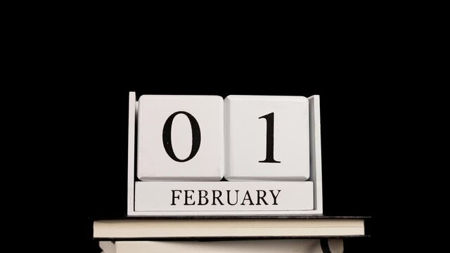 Cube wooden calendar running through the days, on a pile of books, with black background.