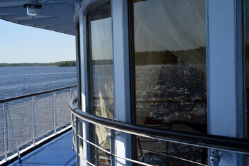 A warm sunny day. In the windows of the restaurant on the ship, the surface of the river is reflected in the sun glare, through the glass you can see a table with dishes.