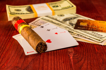 Cuban cigar with playing cards and money with payment card on the table mahogany. Focus on the cuban cigar, identification cards ace Russian letter