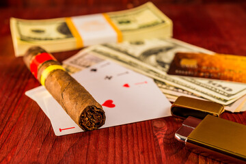 Cuban cigar with playing cards and money with payment card on the table mahogany. Focus on the...