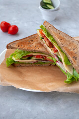 Delicious sandwich with fresh lettuce leaves, tomatoes, cucumbers and cheese on a grey table background.