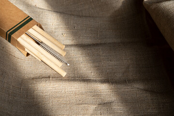 Bamboo eco tubes straws in a cardboard box lie on a canvas in the natural light of the sun in the...