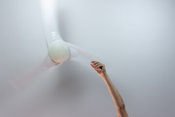 Close-up of hand holding remote control of white ceiling fan. Hand turning on the fan with copy...
